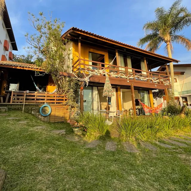 A casa de madeira de dois andares vista do gramado, com redes na varanda